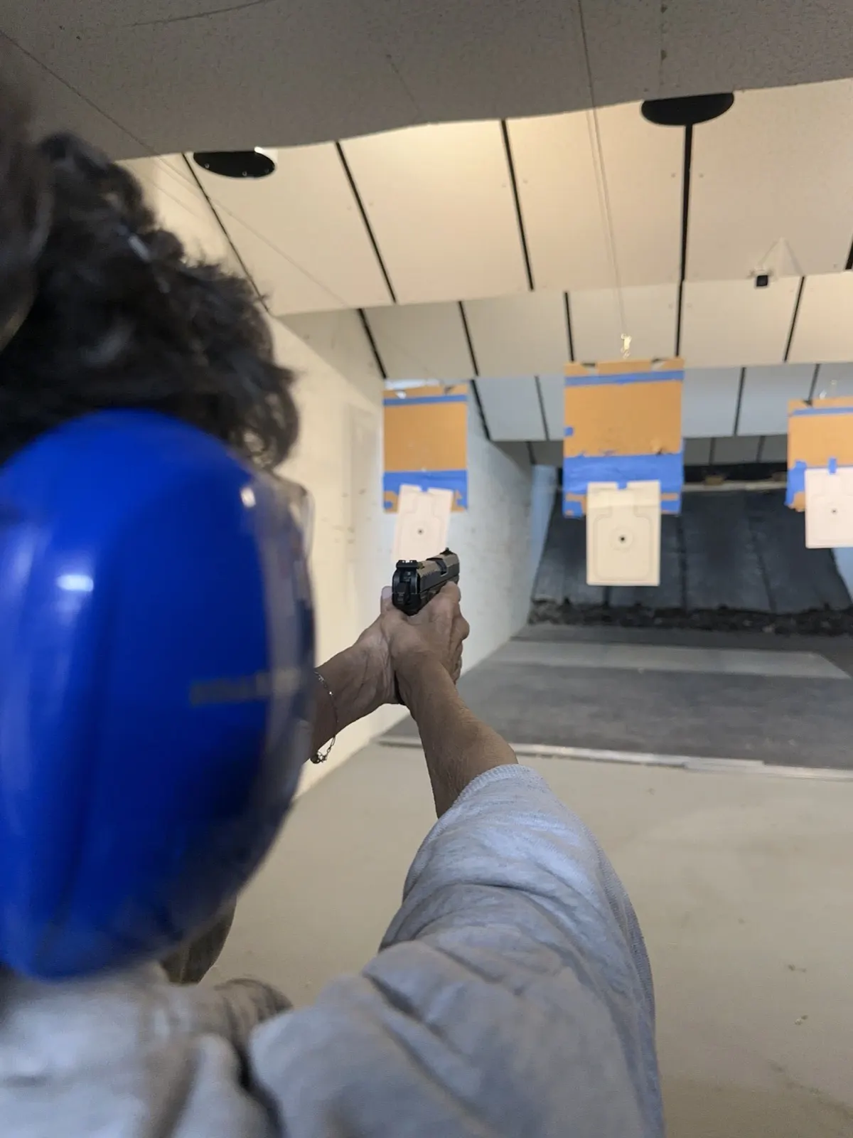 A first-timer on her own lane, aiming a pistol downrange at a paper target.