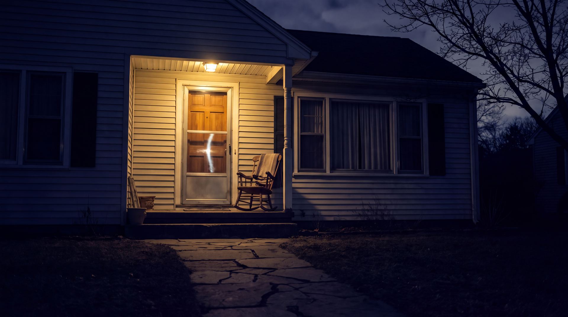A porch light burning over the front door of a New England home at night